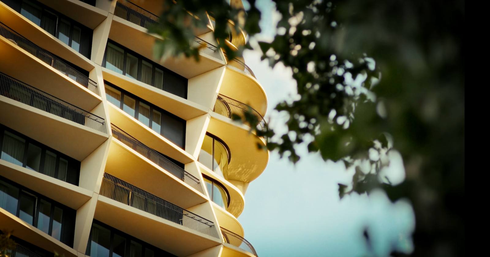 Detail van een gebogen, gouden balkongevel tussen het groen